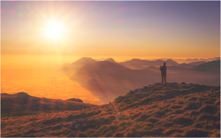 man standing on mountain edge looking at sunset